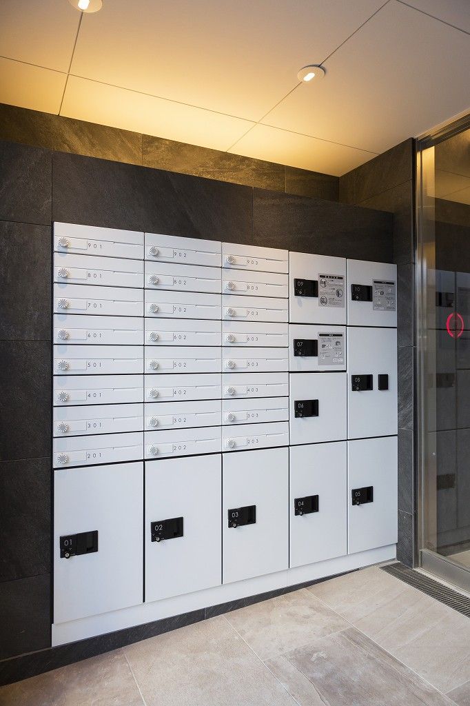 A row of white lockers with numbered compartments, a glass door to the right, and a tiled floor.