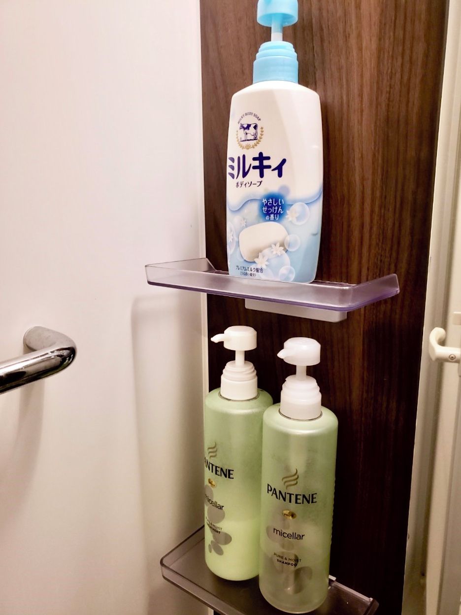 A bathroom with a mirror, a shelf holding a bottle of shampoo, and two bottles of Pantene hair care products.