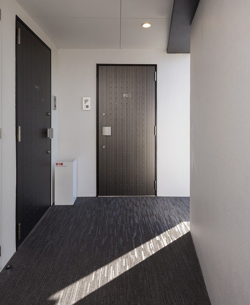 A hallway with a dark wooden door, a white wall, and a small white object on the wall.