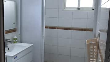 A bathroom with a sink, mirror, and shower. There is a window above the shower, and a mat with London landmarks on the floor.