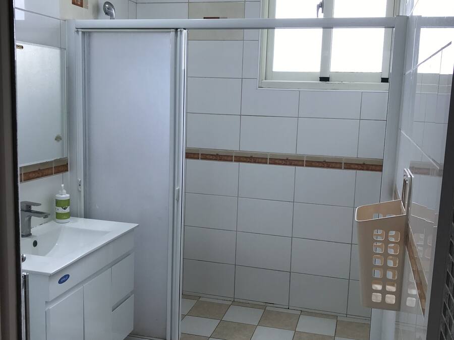 A bathroom with a sink, mirror, and shower. There is a window above the shower, and a mat with London landmarks on the floor.