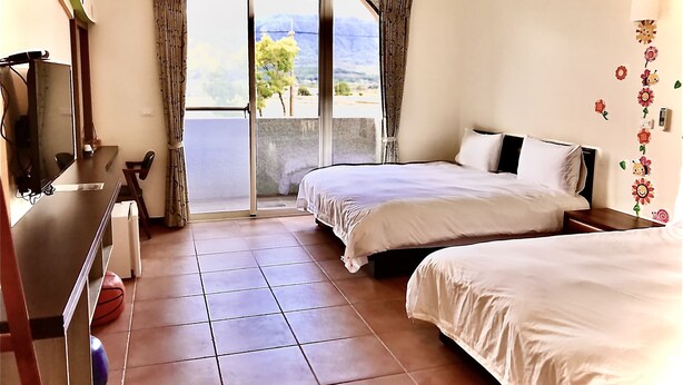 A hotel room with two beds, a desk with a chair, a large window with curtains, and a view of the outdoors. - Min Min Bed and Breakfast (Chishang)