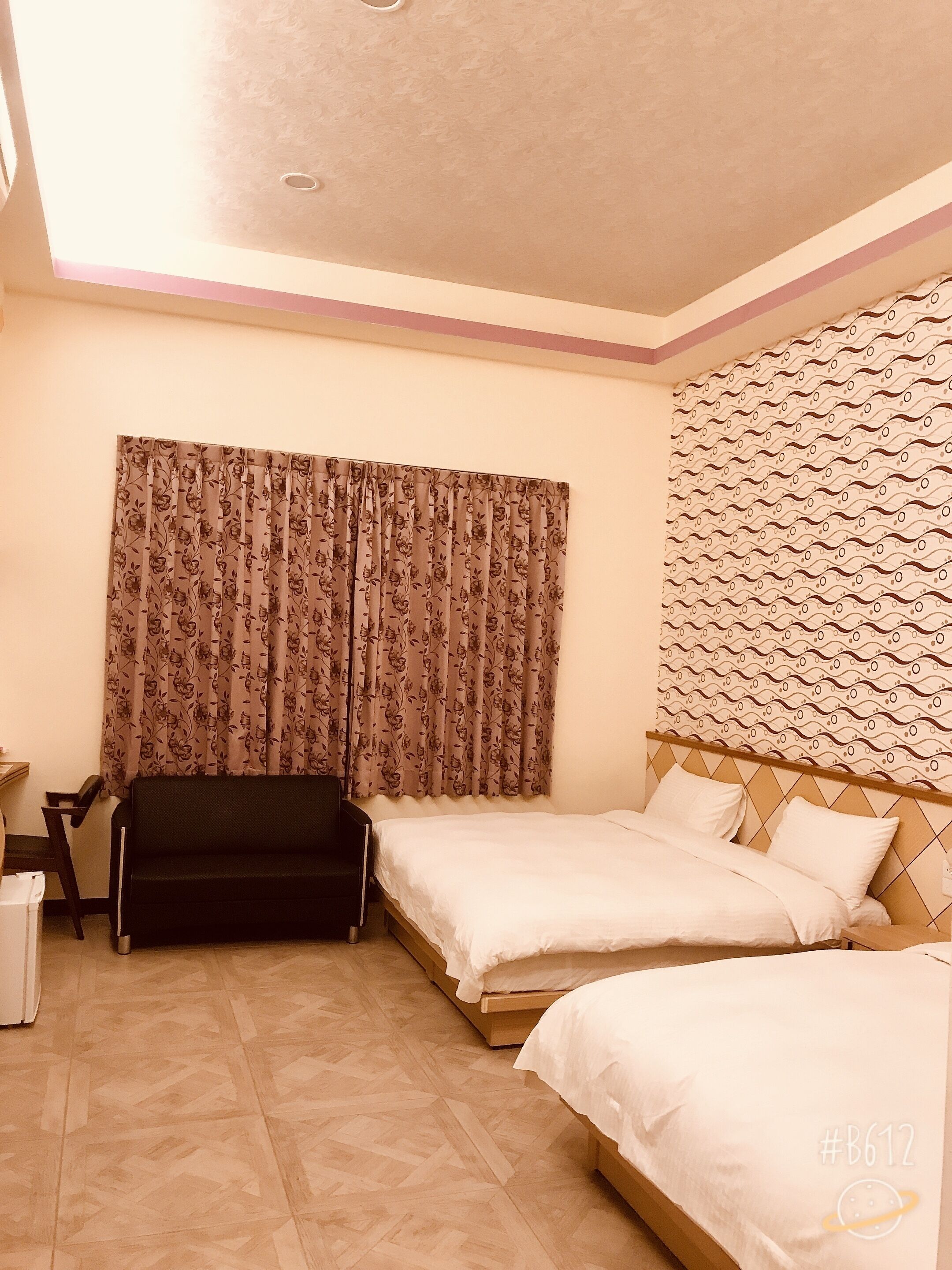 A hotel room with two beds, a sofa, a desk, and a patterned curtain.