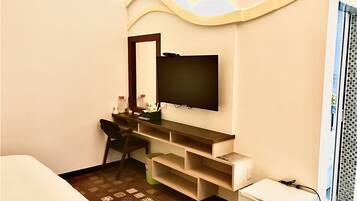Habitación de hotel con televisión montada en la pared, escritorio con silla, refrigerador pequeño y ventana con vista a la ciudad.