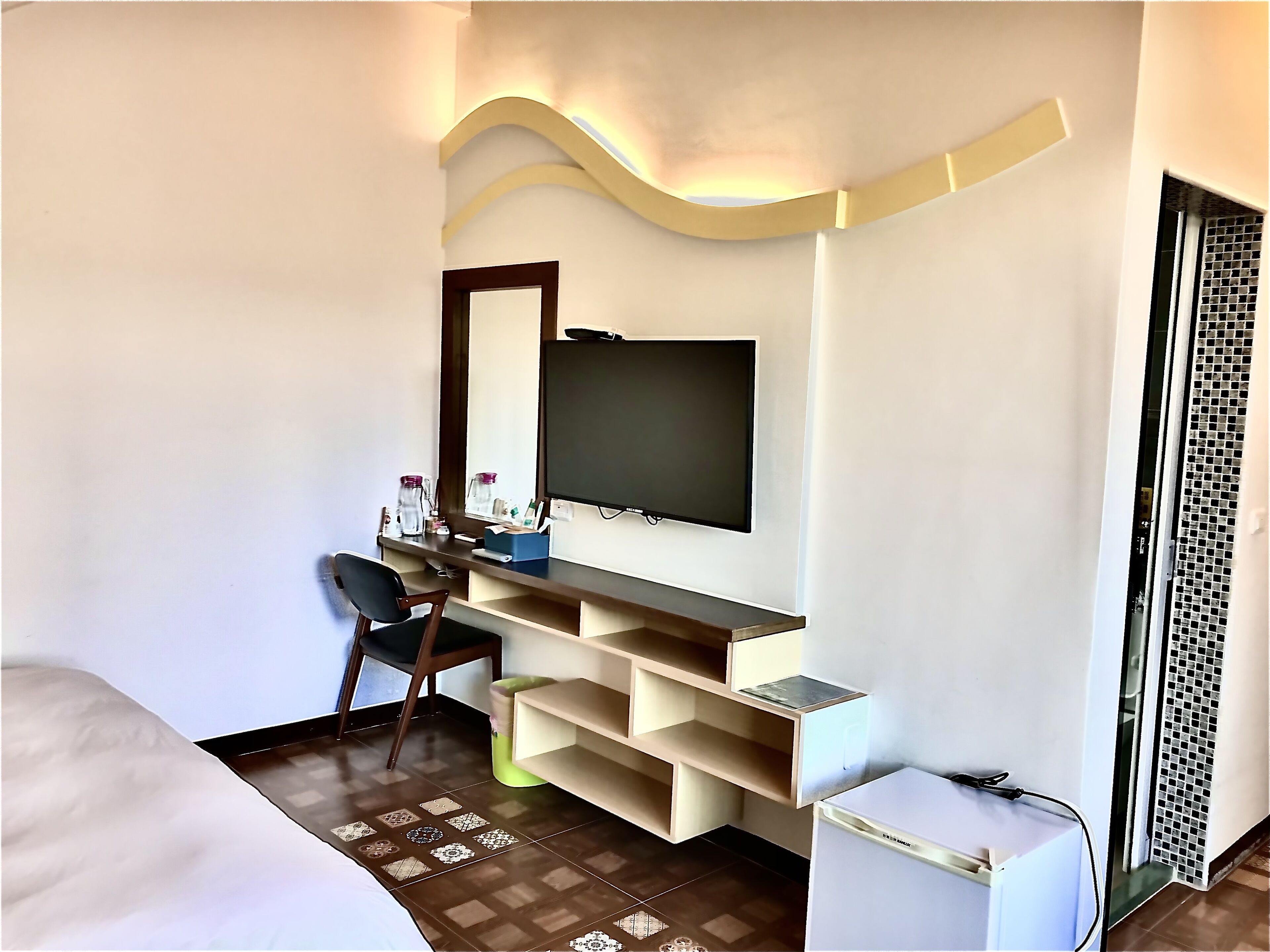 A hotel room with a bed, a desk with a chair, a television, and a small refrigerator.