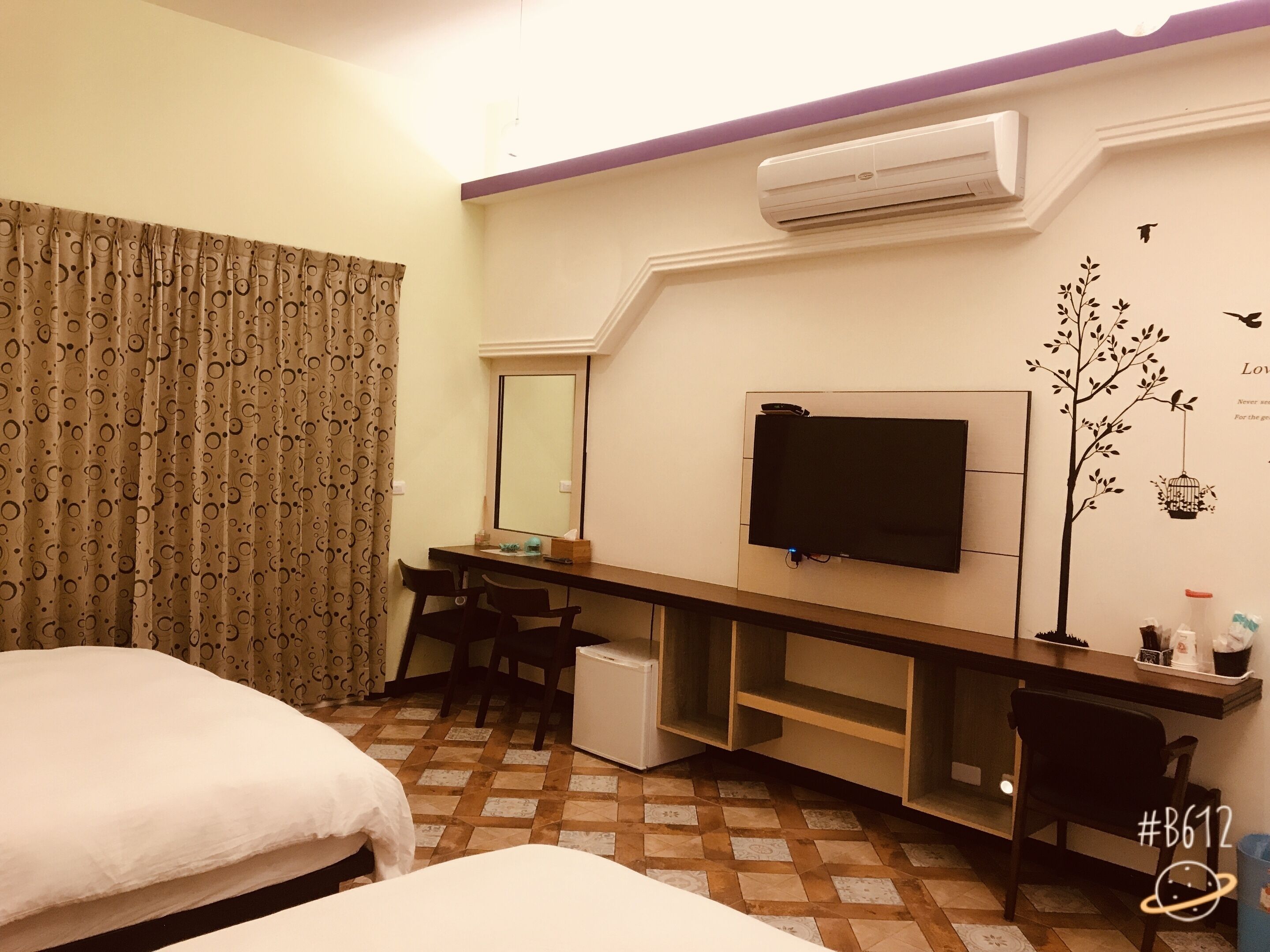 A hotel room with a bed, a desk with a chair, a television, and an air conditioning unit.