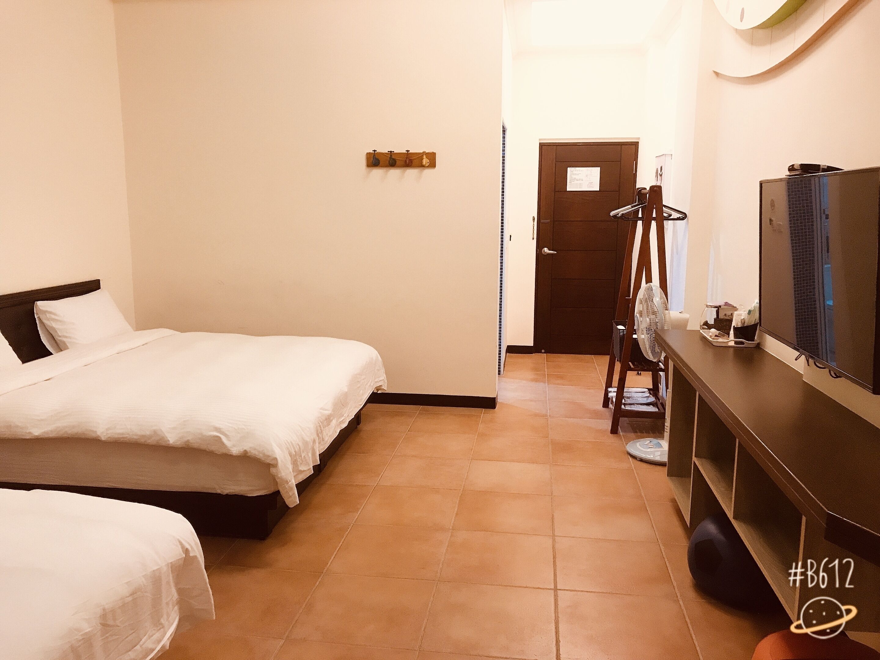 A hotel room with two beds, a desk with a television, and a door leading to another room.