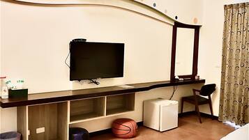 A hotel room with a flat-screen TV, a small refrigerator, a basketball, a chair, and a ceiling fan.