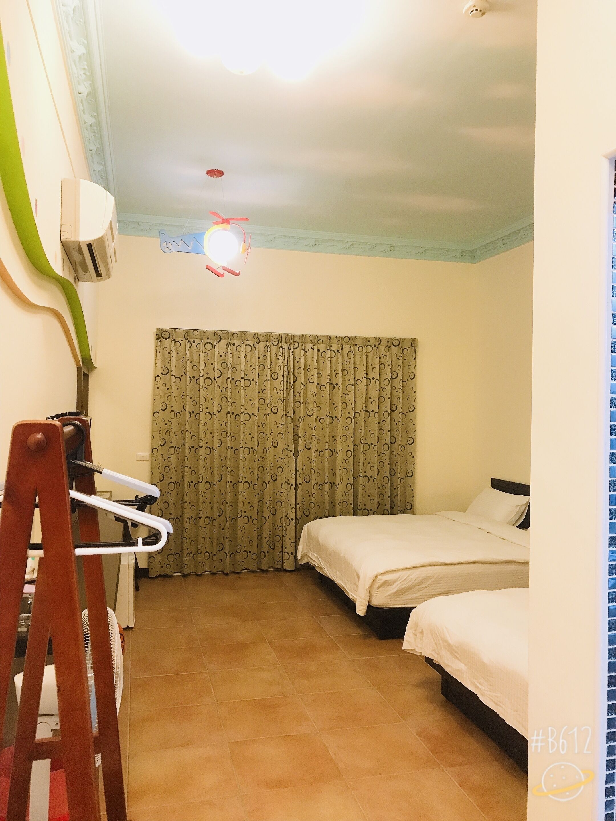 Una habitación pequeña y luminosa con dos camas, un ventilador de techo y una ventana con cortinas.