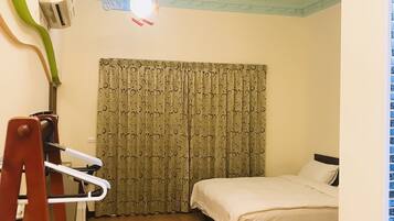 Una habitación pequeña y luminosa con dos camas, un ventilador de techo y una ventana con cortinas.