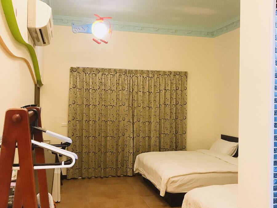 Una habitación pequeña y luminosa con dos camas, un ventilador de techo y una ventana con cortinas.