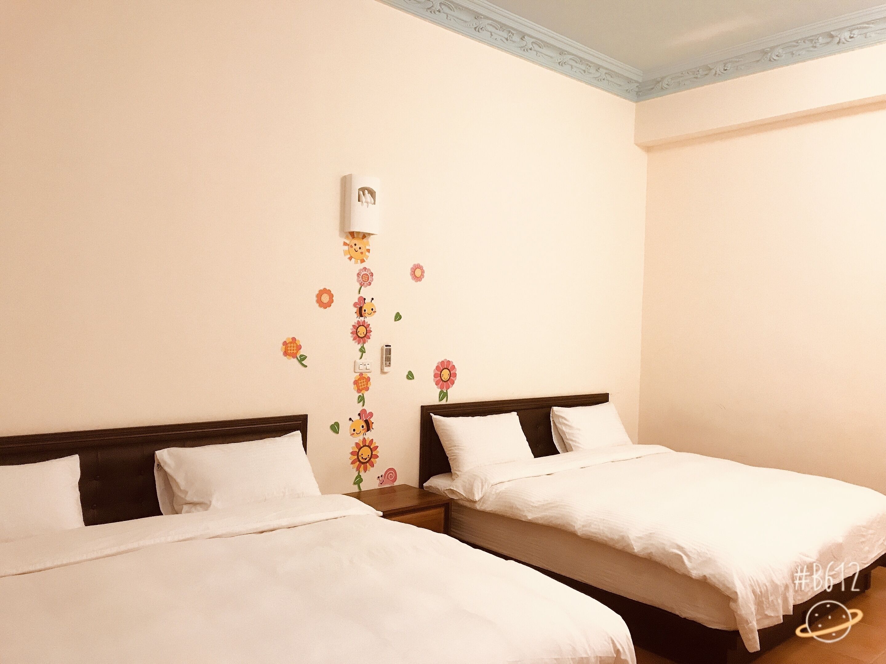 A hotel room with two beds, a wall-mounted air conditioner, and a decorative floral wall decal.