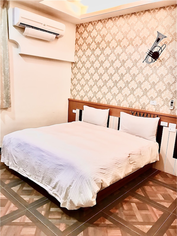 A neatly made bed with a white comforter and pillows, a wooden headboard, a patterned wallpaper, and a wall-mounted air conditioning unit. - Min Min Bed and Breakfast (Chishang)