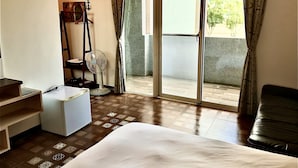 A hotel room with a bed, a desk, a chair, a fan, and a view of the outdoors through a sliding door. - Min Min Bed and Breakfast (Chishang)