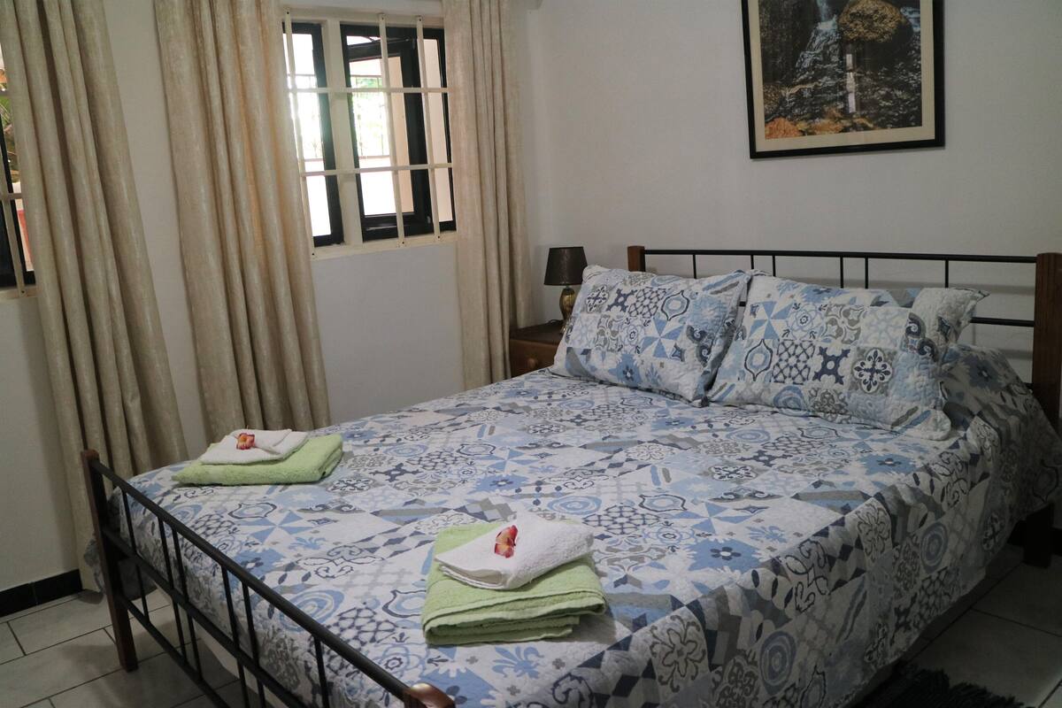 Una camera da letto con un letto, tende, una finestra, un comodino, una lampada e un quadro appeso al muro.