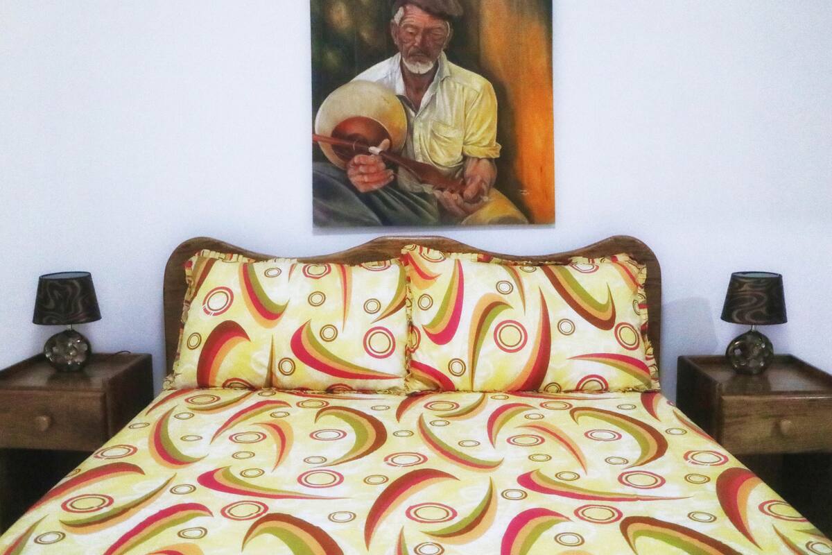 Un letto con una coperta colorata a motivi, due comodini con lampade e un quadro appeso al muro.