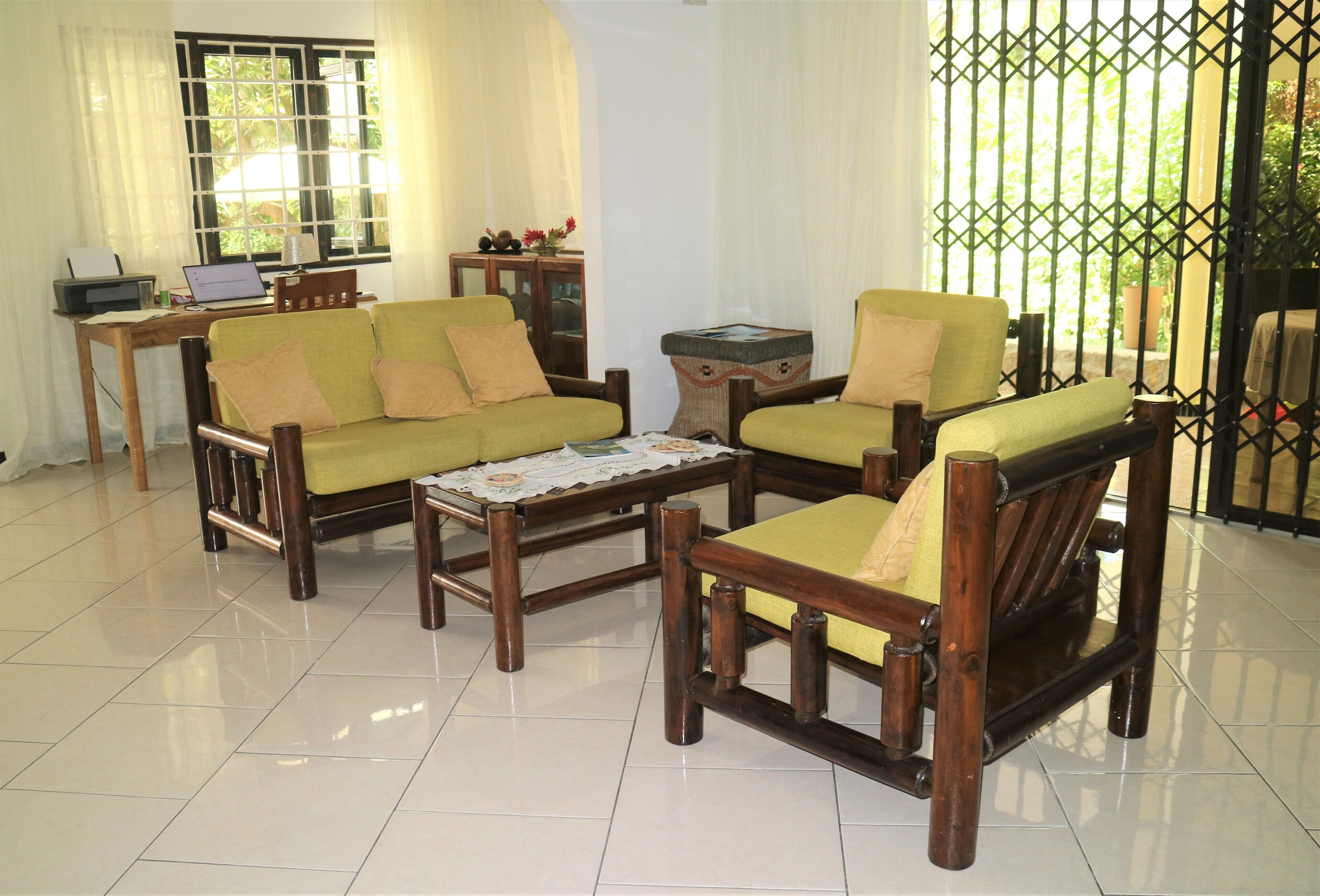 A room with a sofa set, a small table, a laptop on a desk, and a window with curtains.