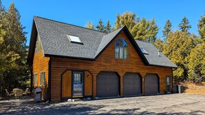 A wooden building with a sloped roof, three garage doors, and a gravel driveway. - Cedar Loft on Lake Michigan (Naubinway)