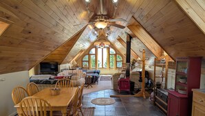 A cozy attic bedroom with a wooden ceiling, a bed, a TV, and a dining area with a table and chairs. - Cedar Loft on Lake Michigan (Naubinway)