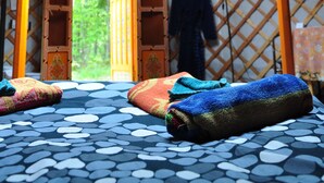 Una yurta con un tragaluz circular, suelo estampado y vistas de vegetación al exterior.