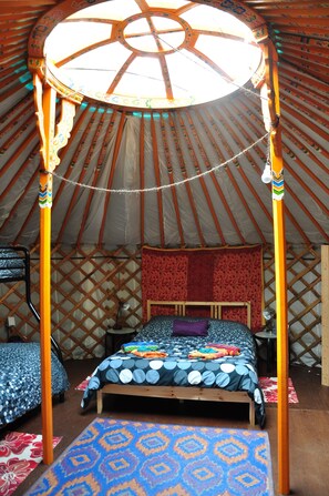 Una yurta con una cama con dosel, alfombras estampadas y suelo de madera.