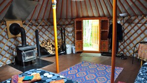 Interior de una yurta con un estufa de calefacción central, un tapete estampado y una puerta de madera que da al exterior.