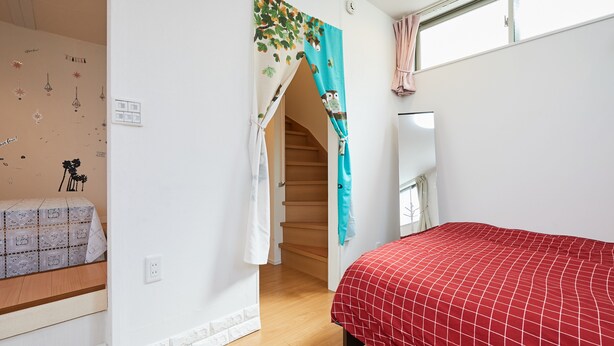A bedroom with a red bedspread, a staircase, and a window with curtains. - Jay and Lan's Himawari house (Tokyo)