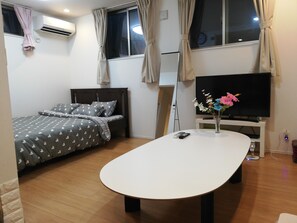 A bedroom with a bed, a TV, a table, and a vase with flowers. - Jay and Lan's Himawari house (Tokyo)