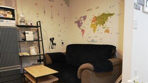 A cozy living room with a world map on the wall, a black sofa, a wooden coffee table, and a metal shelving unit with various items. - Jay and Lan's Himawari house (Tokyo)