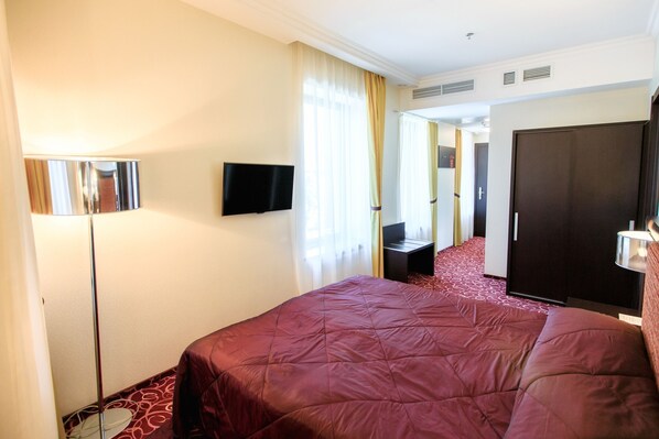 A hotel room with a large bed, a flat-screen TV, a desk, and a wardrobe.