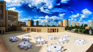An outdoor event space with multiple round tables set up for dining, surrounded by buildings and a clear blue sky with clouds. - Menorah Hotel (Dnipro)