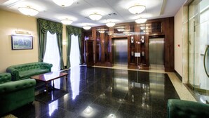 A lobby with a green sofa, a wooden reception desk, and a modern elevator. - Menorah Hotel (Dnipro)