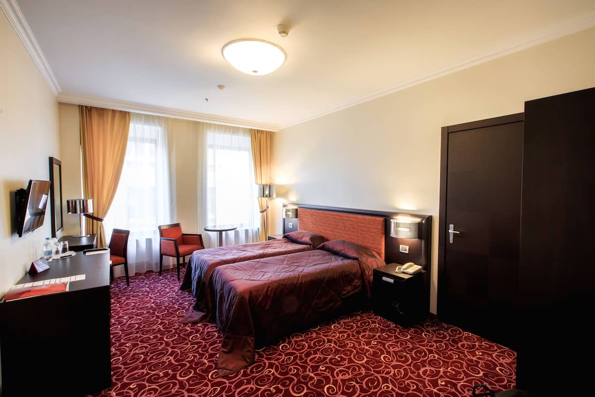 Una habitación de hotel con dos camas, un escritorio, una silla, una lámpara y un armario.