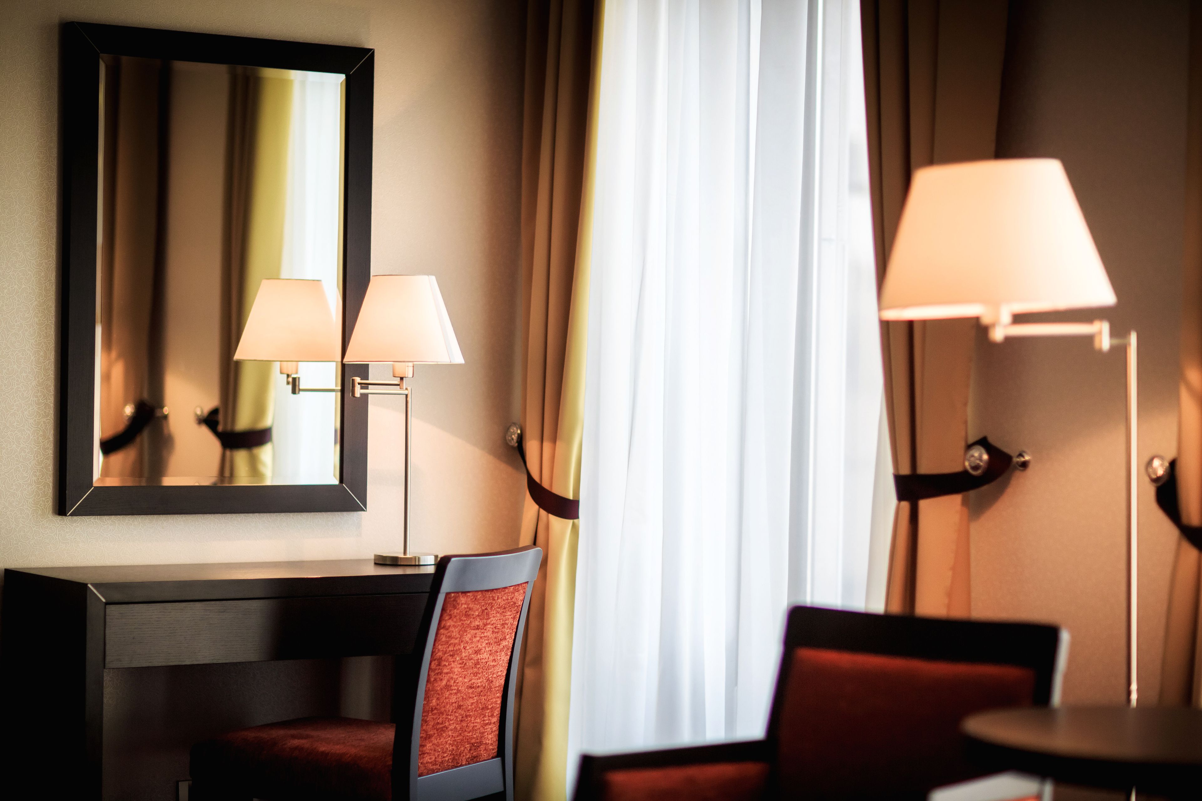 A hotel room with a desk, two chairs, a mirror, and two lamps.