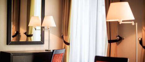 A hotel room with a desk, two chairs, a mirror, and two lamps.