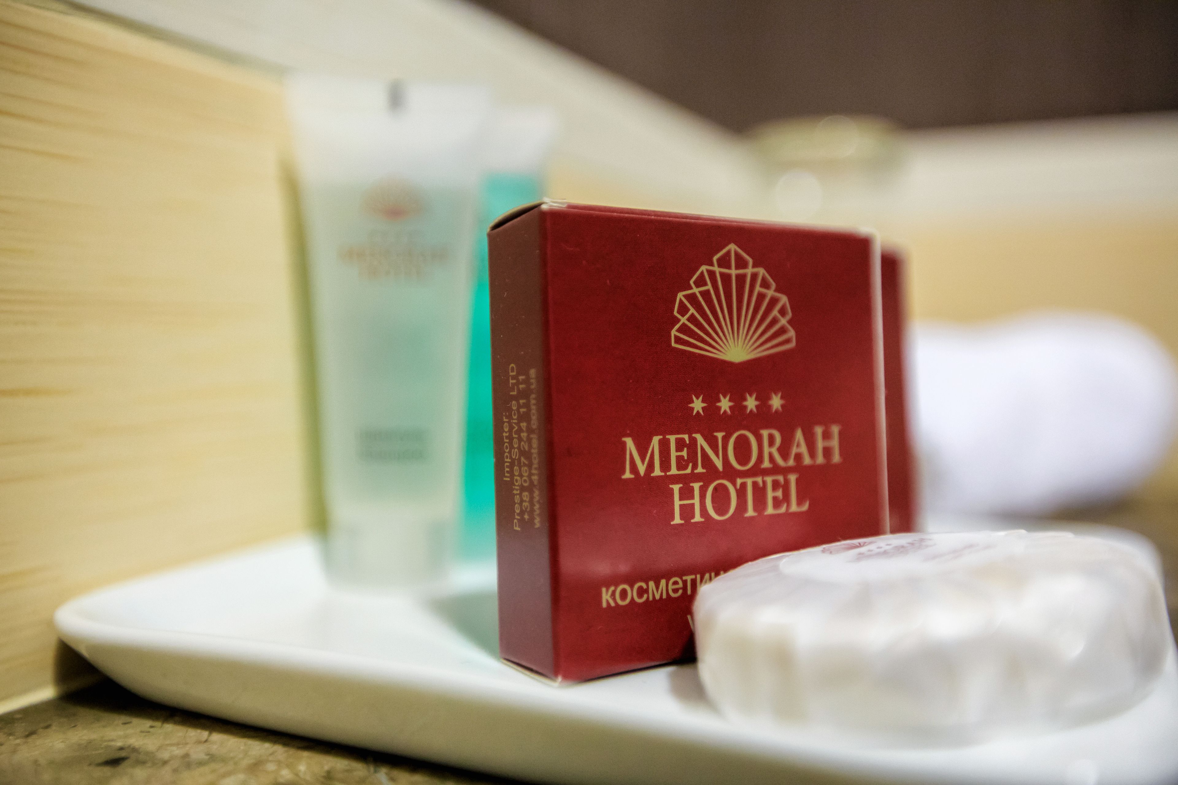 Una pastilla de jabón con la marca Menorah Hotel y una caja roja con el logo del hotel sobre una bandeja blanca.