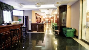 A hotel lobby with a reception desk, bar area, seating, and a glass-enclosed shower area. - Menorah Hotel (Dnipro)