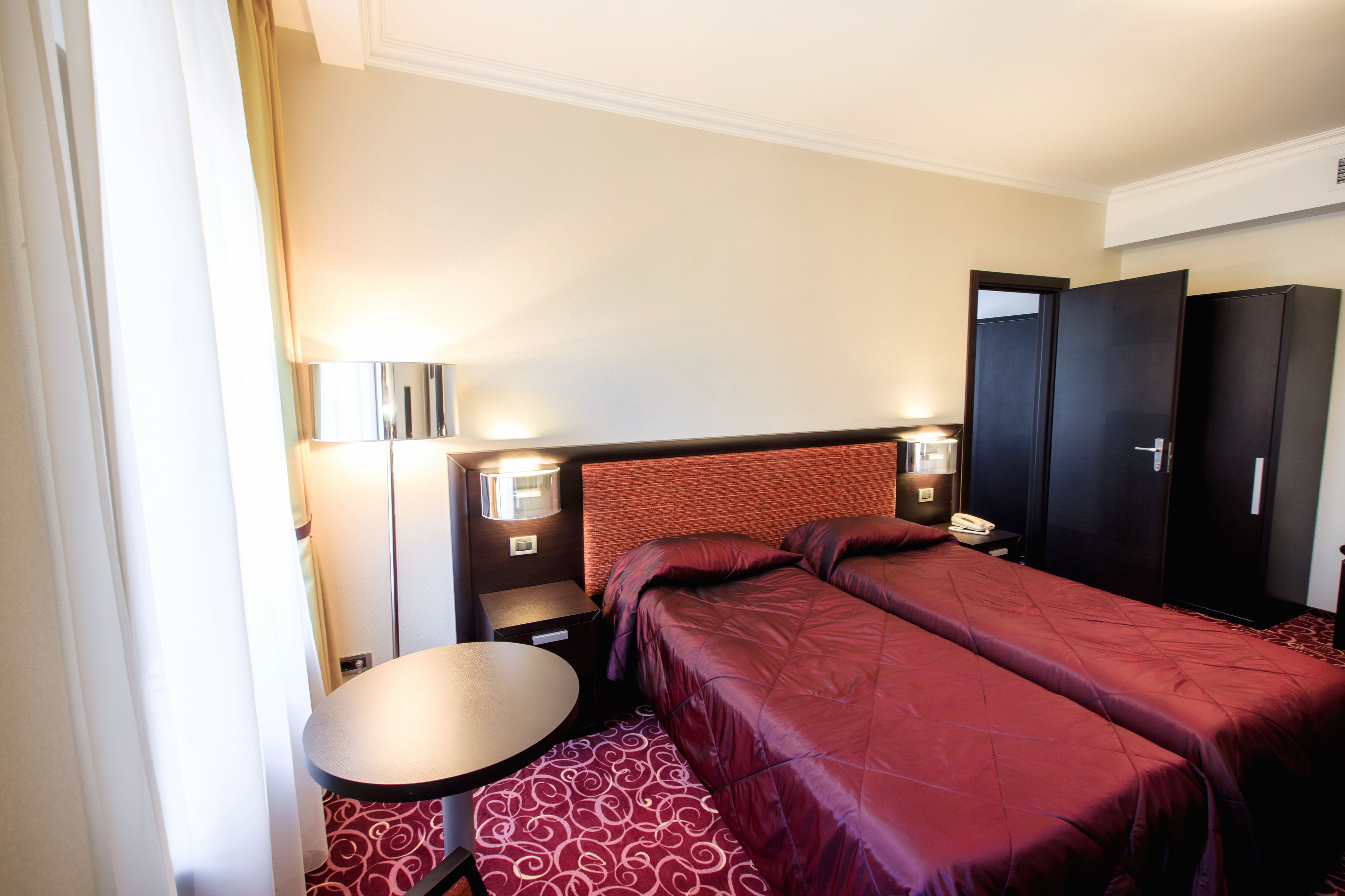 A hotel room with two beds, a small table, a lamp, a wardrobe, and a telephone.