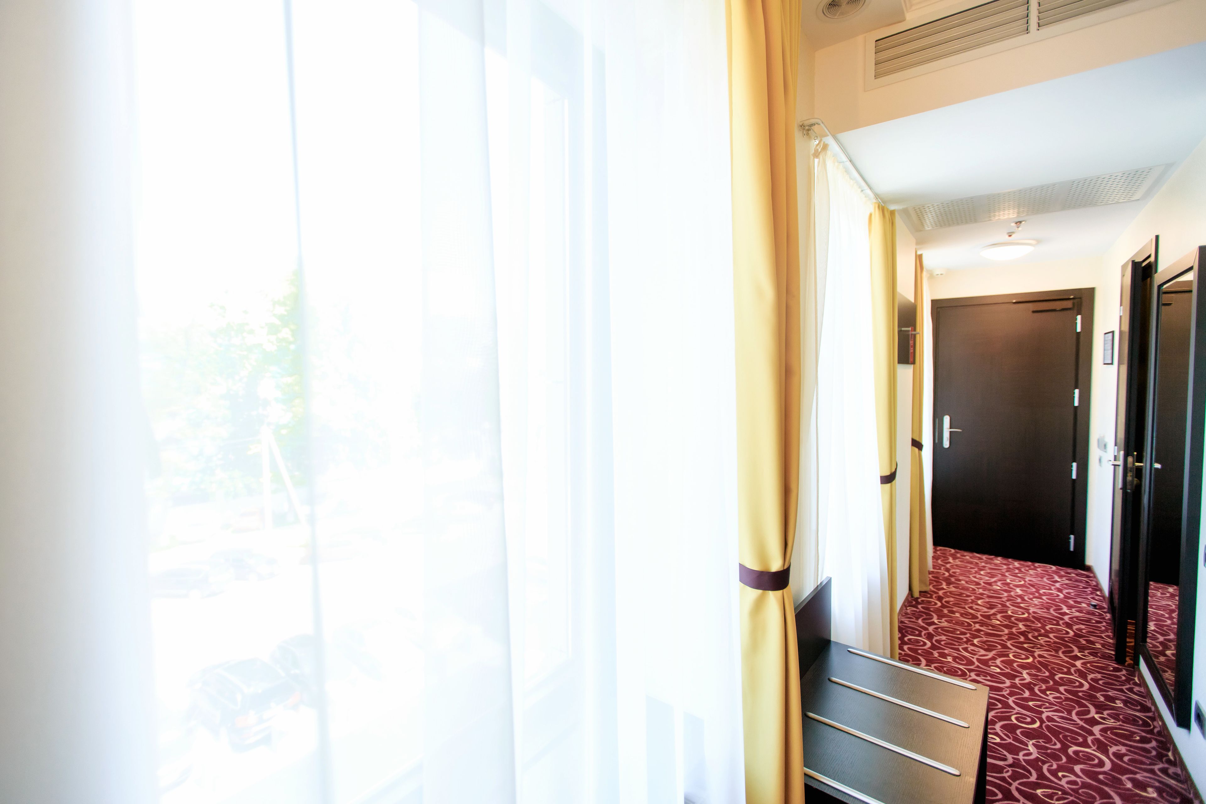 A hotel hallway with a bench, a door, and a window with curtains.