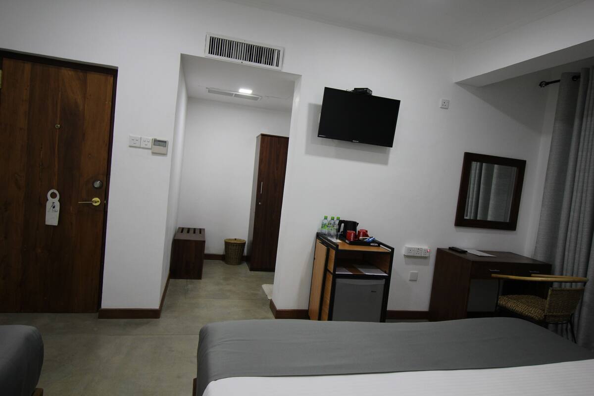 A hotel room with a bed, a desk, a chair, a television, and a wardrobe.