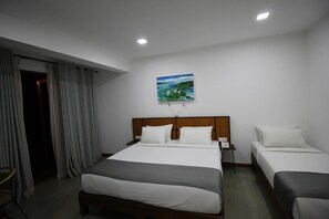 A hotel room with a large bed, two bedside tables, a painting on the wall, and a window with curtains. - Serenity Tissa (Thissamaharama)