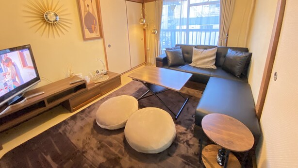 A modern living room with a sofa, ottomans, a TV, and a sunburst wall decoration. - Shibuya Japanese-style room 2DK small up to family 4 parsons + Pocket Wifi (渋谷区)