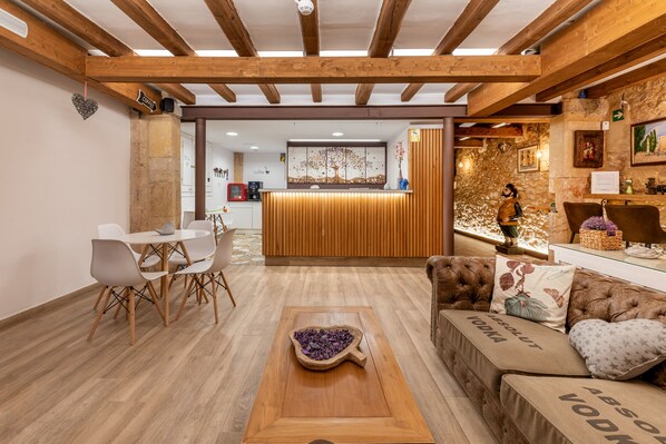 A cozy lobby with wooden beams, a reception desk, a coffee machine, and a seating area with a sofa and chairs.