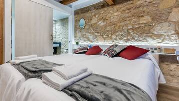 A bedroom with a stone wall, a bed with white linens, a red pillow, and a wooden ceiling.