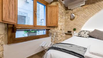 Un dormitorio con pared de piedra, armarios de madera, una cama con edredón blanco, un reloj y una pequeña planta en maceta.