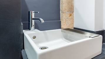 A white rectangular sink with a chrome faucet, set against a dark wall with a textured beige accent.