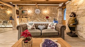 A cozy room with a stone wall, a sofa with 'Absolut Vodka' pillows, a wooden coffee table with a potted plant and a decorative bowl. - Hostal 977 (Tarragona)