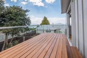 A wooden deck with a view of a building and a tree. - Lakeside Gem - Lake Views, Kayaks, Sleeps 8 (Rotorua)
