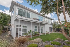 A modern two-story house with a covered patio, a well-maintained lawn, and a variety of plants. - Lakeside Gem - Lake Views, Kayaks, Sleeps 8 (Rotorua)