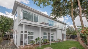 Ein modernes, zweistöckiges Haus mit großen Glasfenstern, einem gepflegten Rasen und verschiedenen Pflanzen.